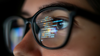 A designer looking at a computer screen and code is reflected in her glasses.